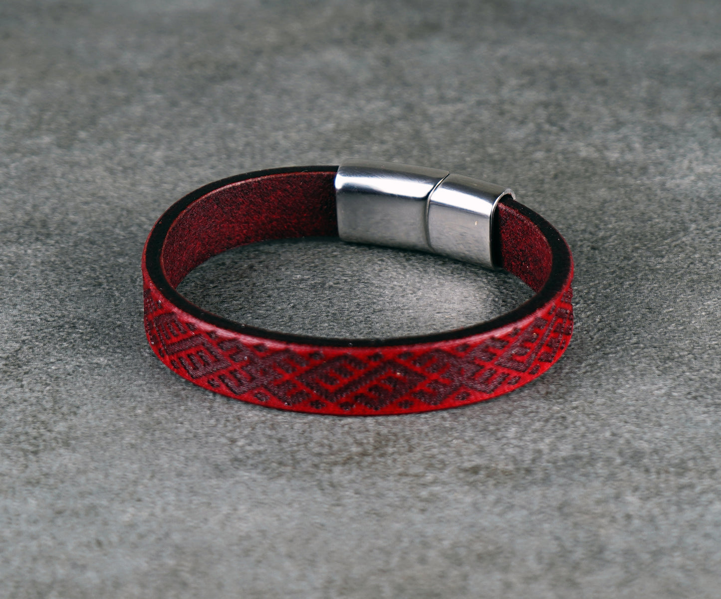 Red leather bracelet with a silver clasp on a gray surface