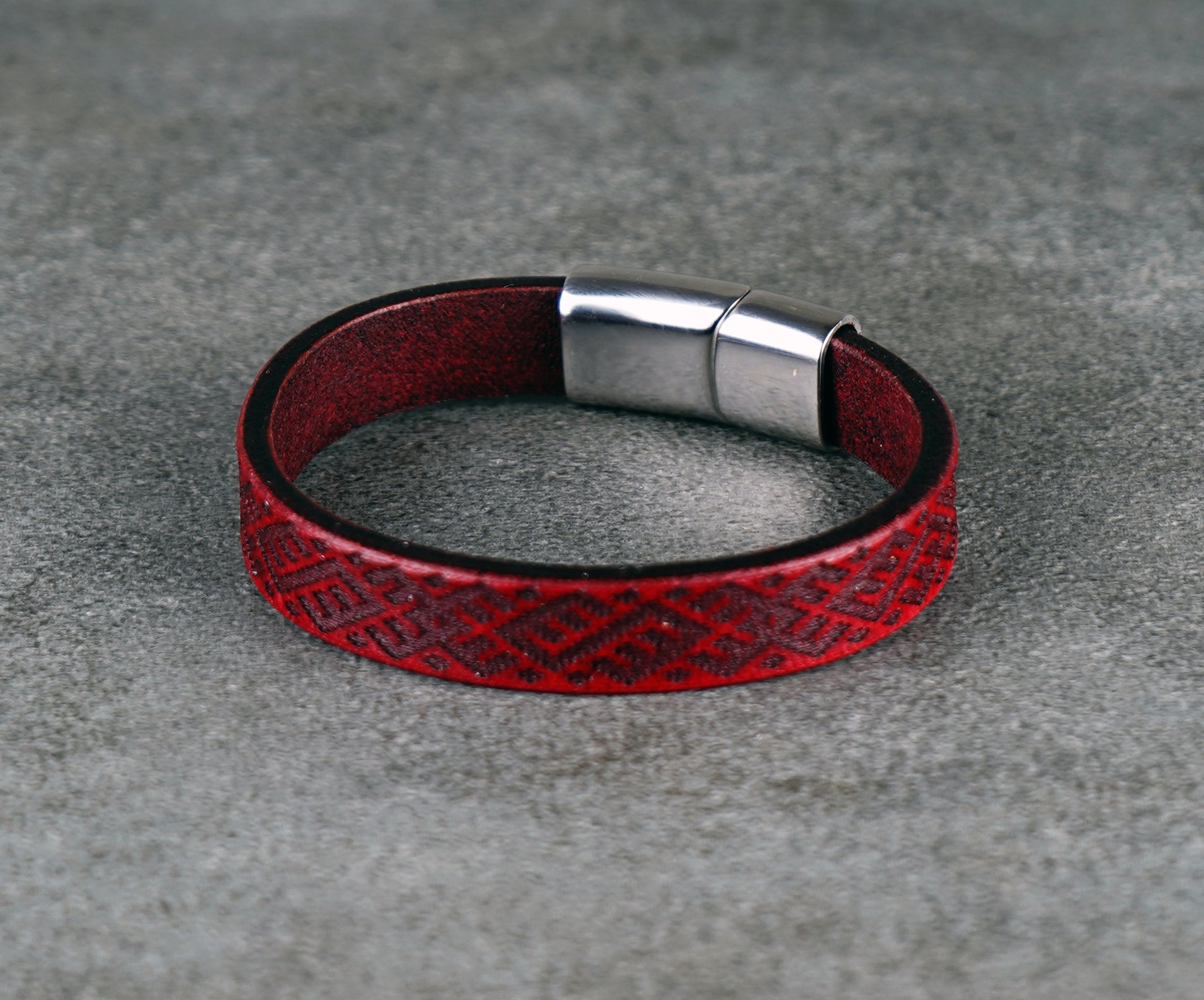 Red leather bracelet with a silver clasp on a gray surface