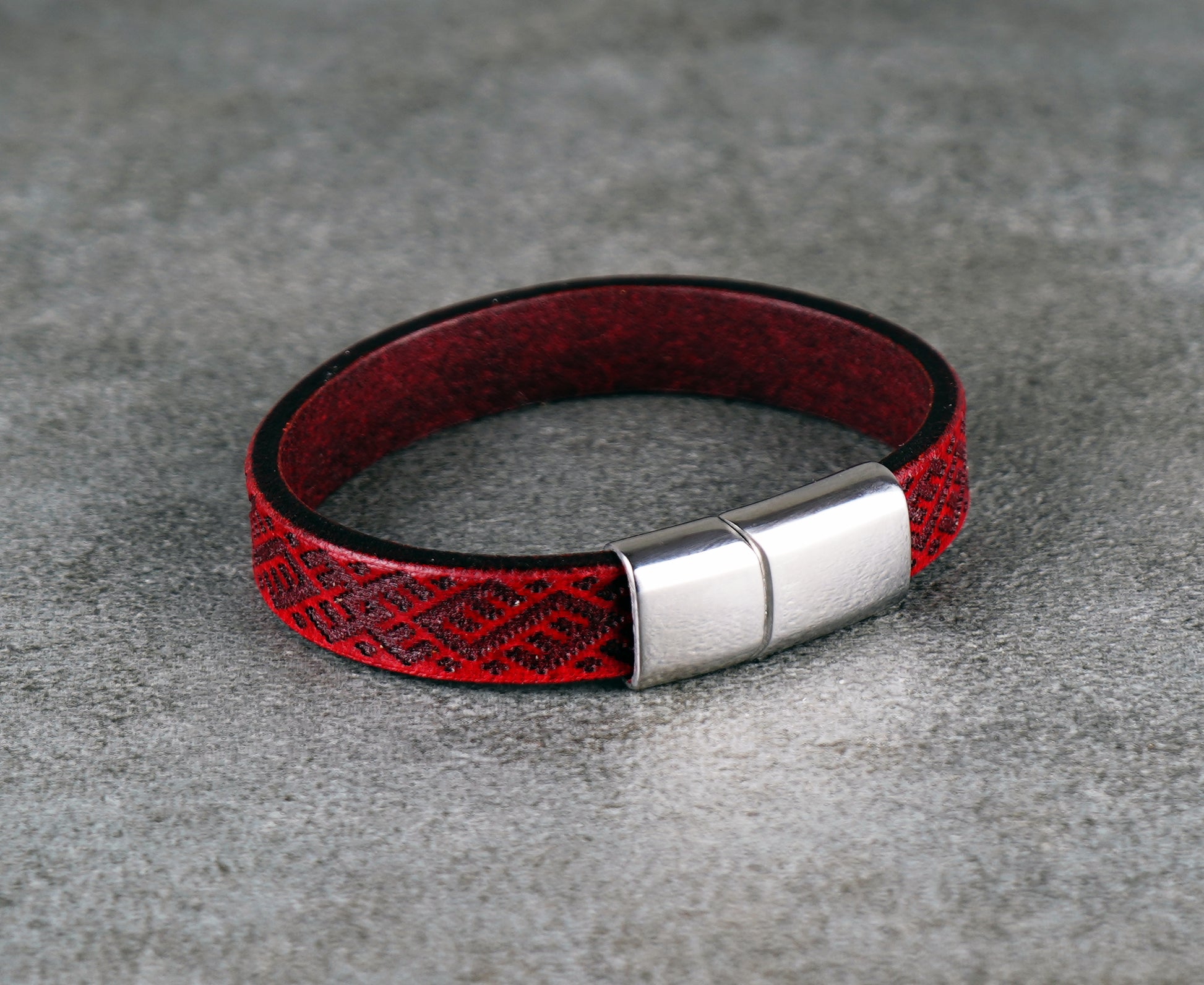Red leather bracelet with a silver clasp on a gray surface