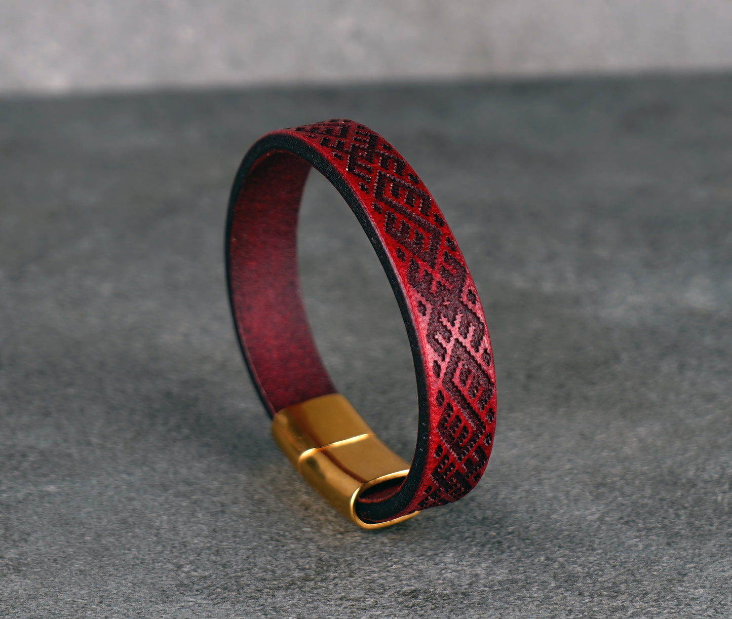 Red leather bracelet with gold clasp on a gray background