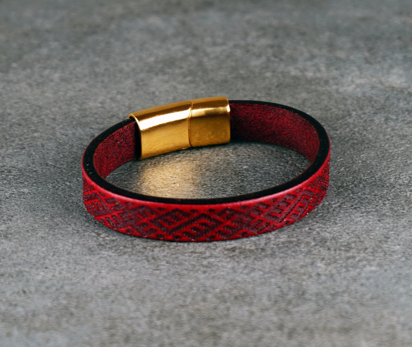 Red leather bracelet with gold clasp on a gray surface