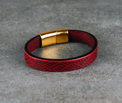 Red leather bracelet with gold clasp on a gray surface