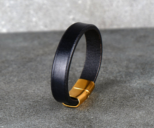 Black leather bracelet with a gold clasp on a gray surface