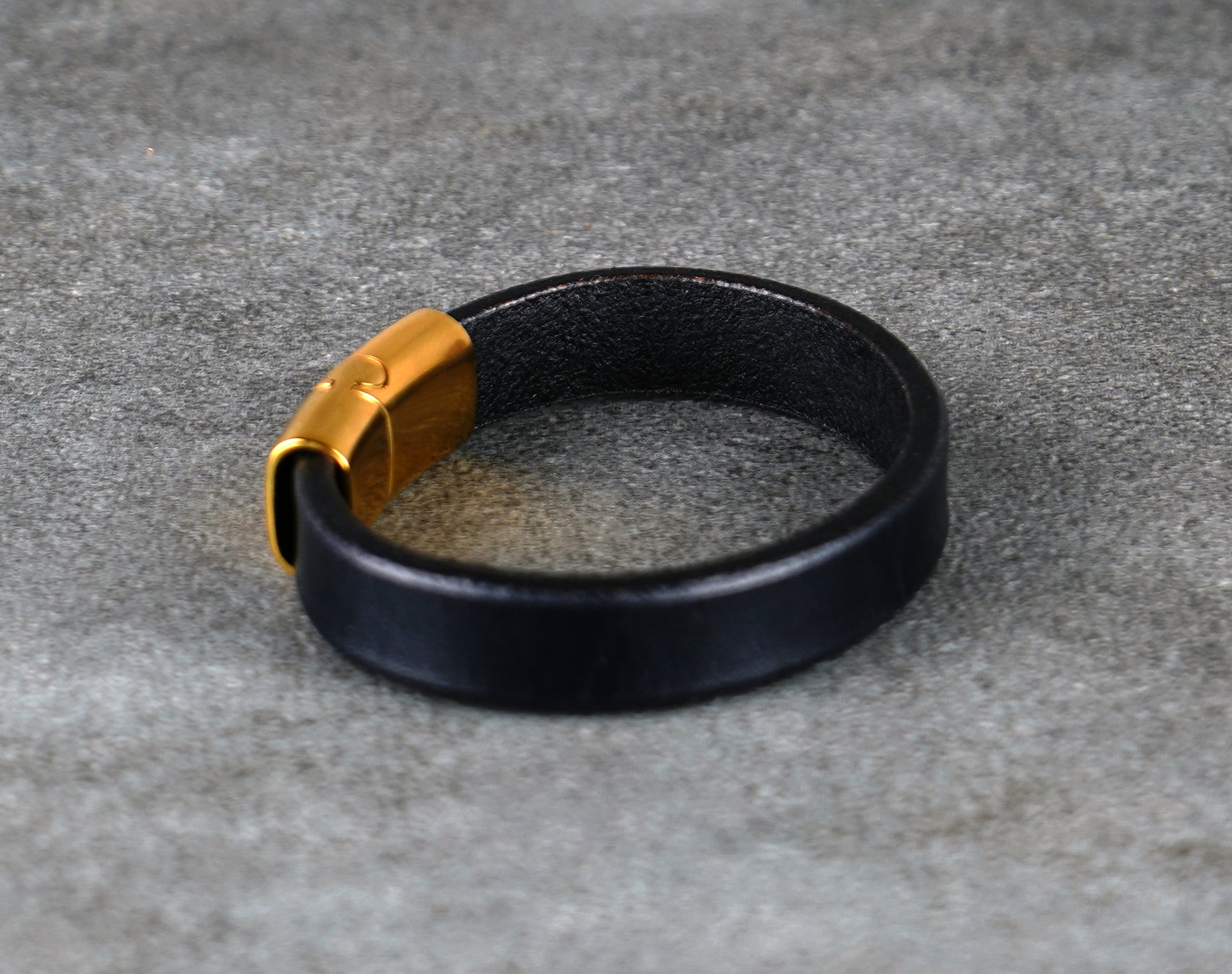 Black leather bracelet with a gold clasp on a gray surface