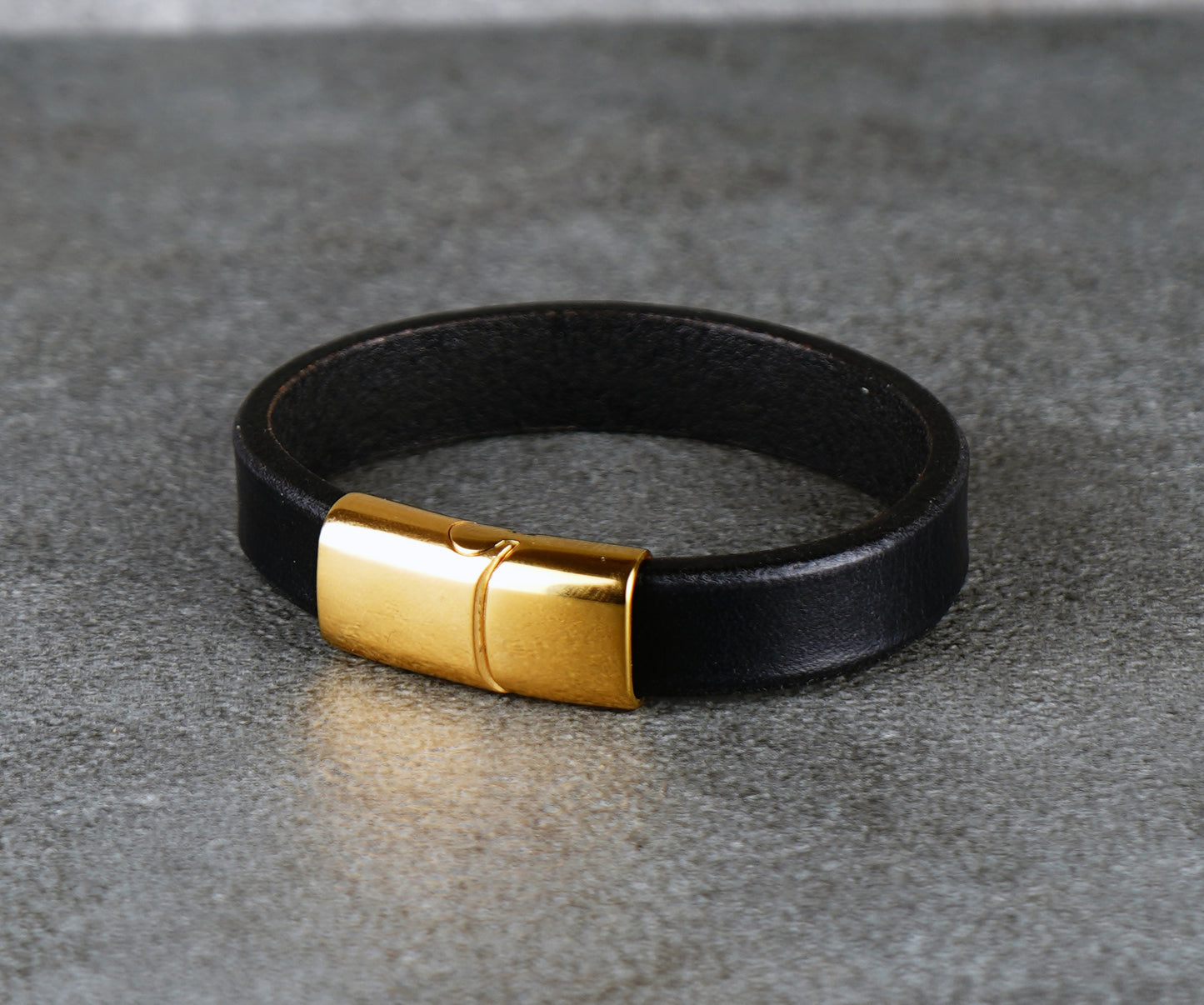 Black leather bracelet with a gold clasp on a gray surface