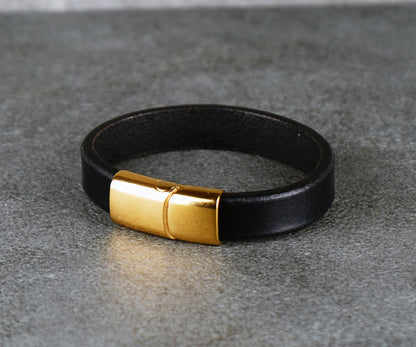 Black leather bracelet with a gold clasp on a gray surface