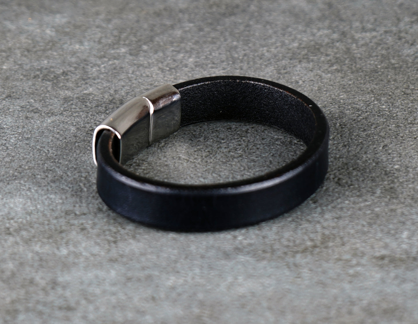 Black leather bracelet with a silver clasp on a gray concrete surface