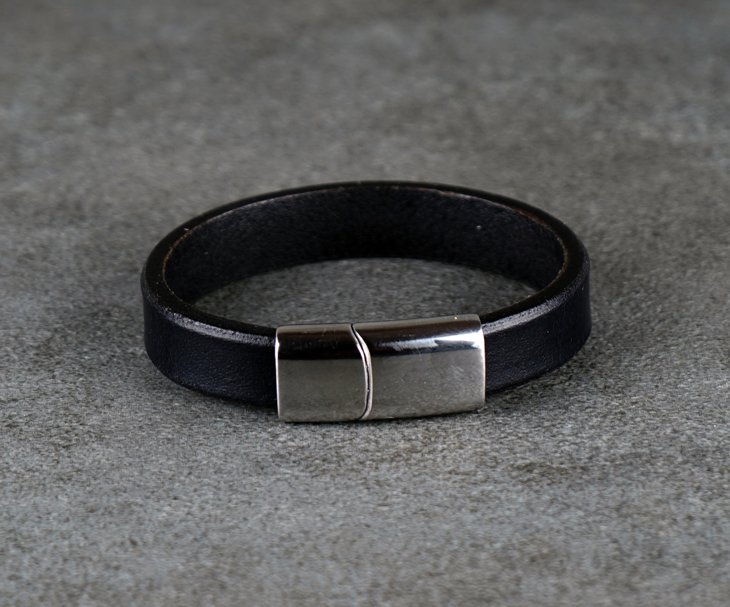 Black leather bracelet with a silver clasp on a gray surface