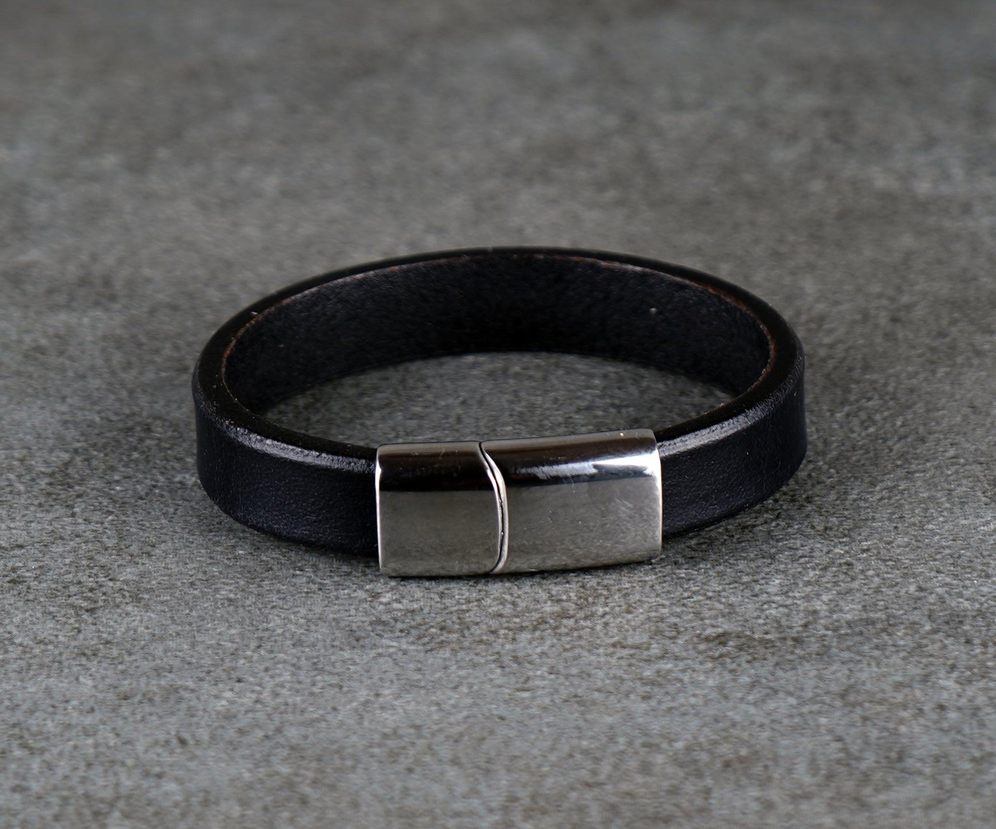 Black leather bracelet with a silver clasp on a gray surface