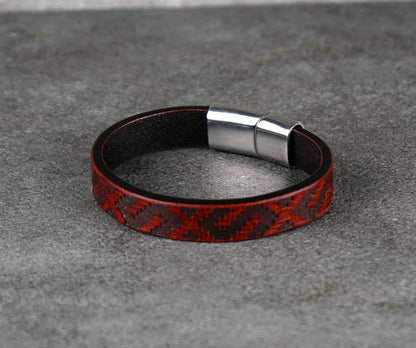 Red and black patterned leather bracelet with a silver clasp on a gray surface