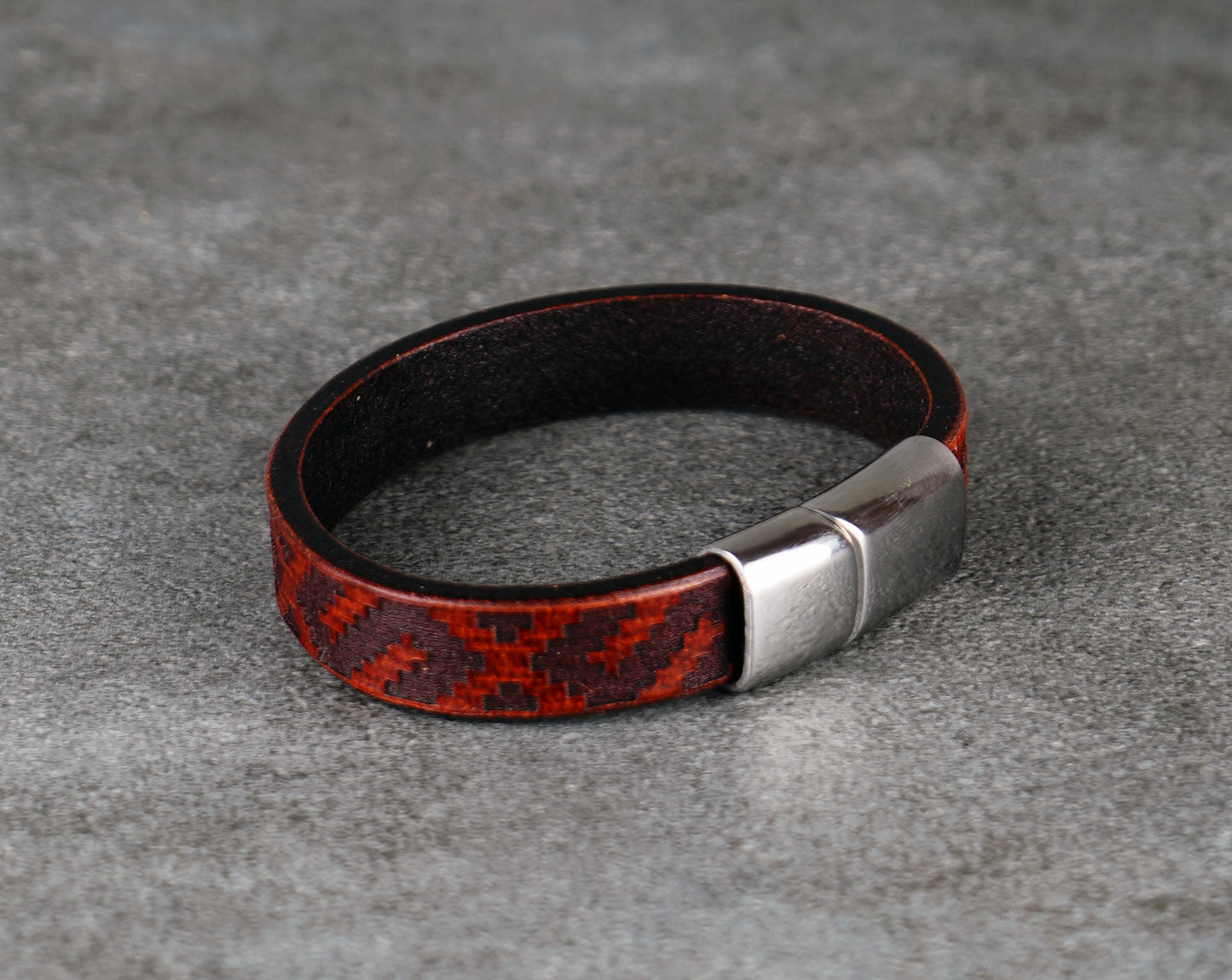 Black and red patterned leather bracelet with a silver clasp on a gray surface