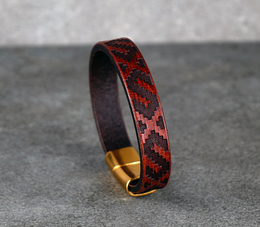 Leather bracelet with geometric pattern and gold clasp on a gray background