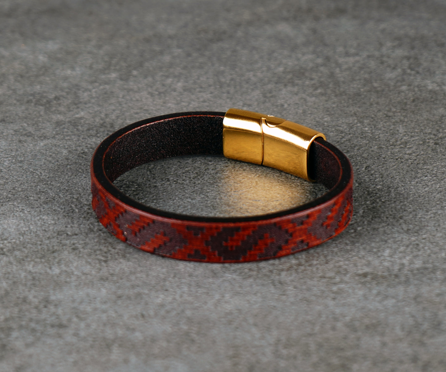Leather bracelet with red pattern and gold clasp on a gray surface