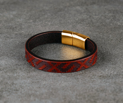 Leather bracelet with red pattern and gold clasp on a gray surface