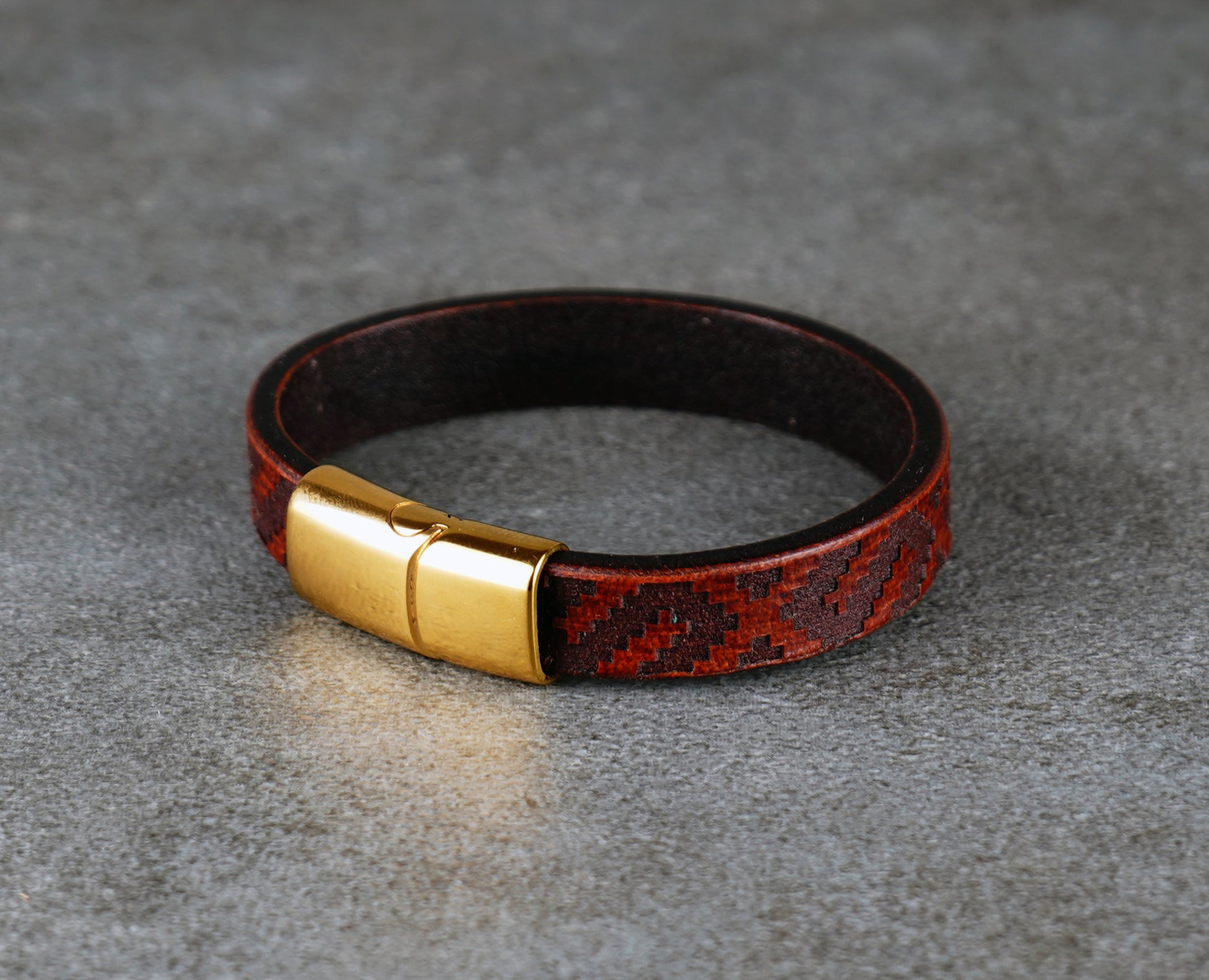 Brown leather bracelet with gold clasp on a gray surface