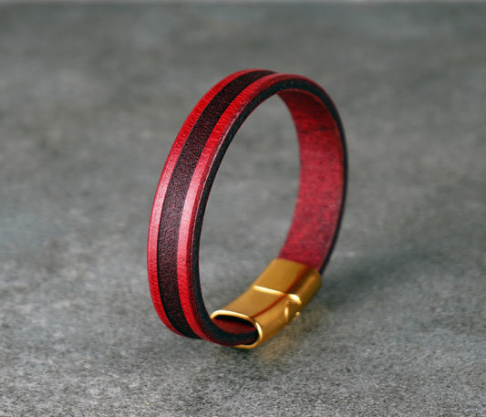 Red and black leather bracelet with a gold clasp on a gray surface
