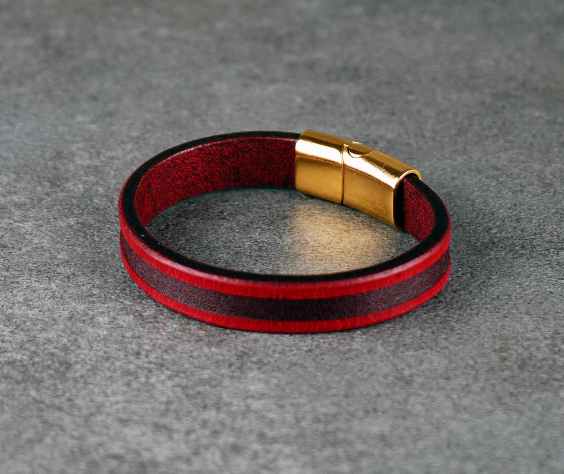 Red and black leather bracelet with a gold clasp on a gray surface