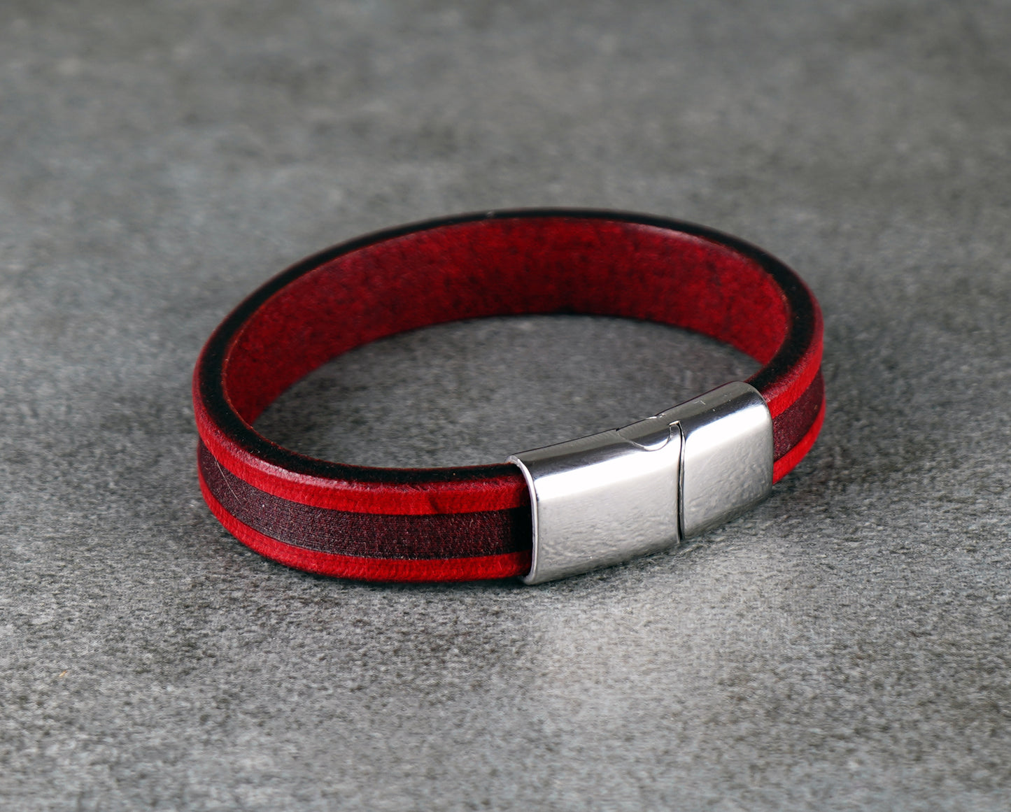 Red and black leather bracelet with a silver clasp on a gray surface