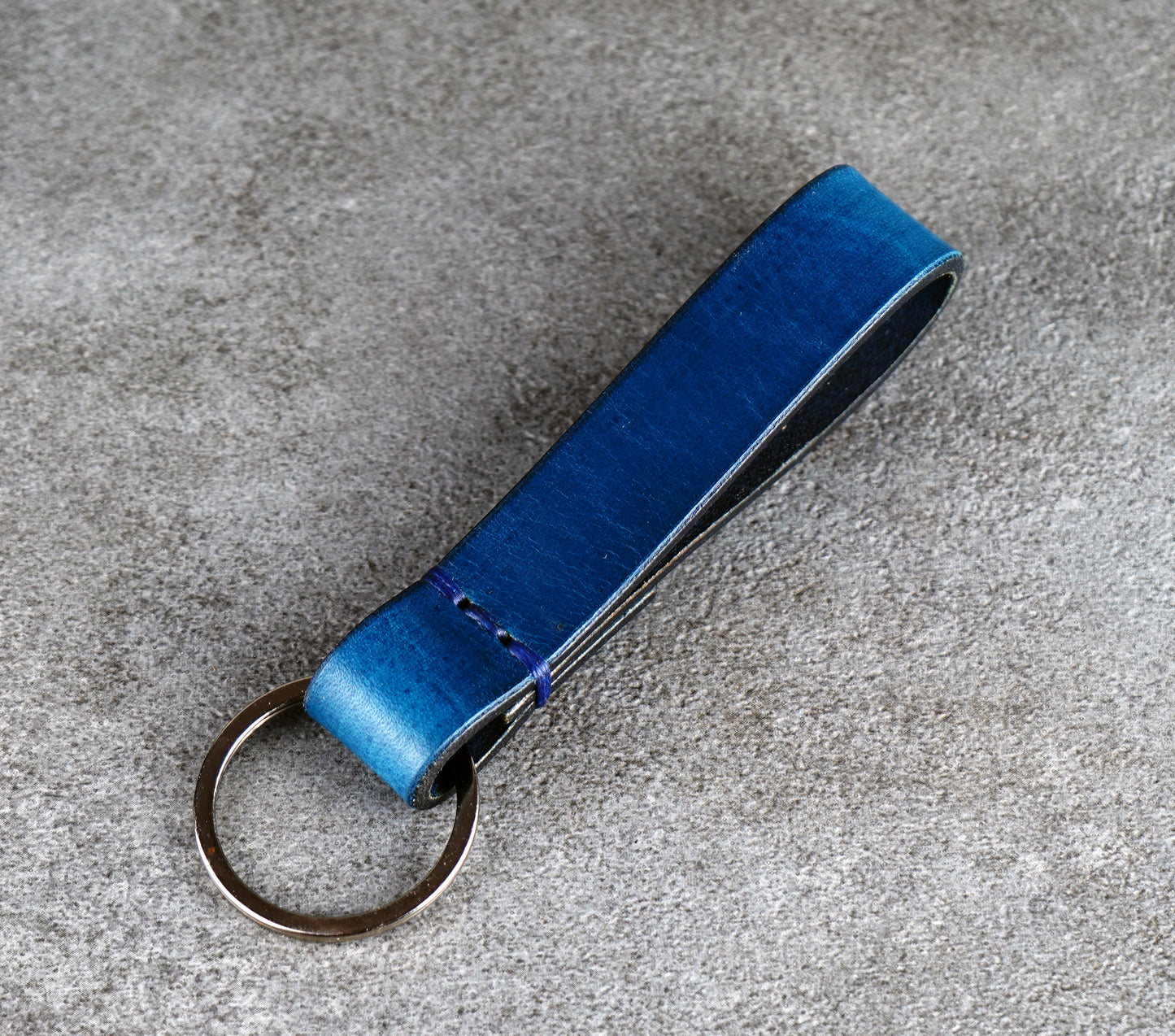 Blue leather keychain on a gray concrete surface