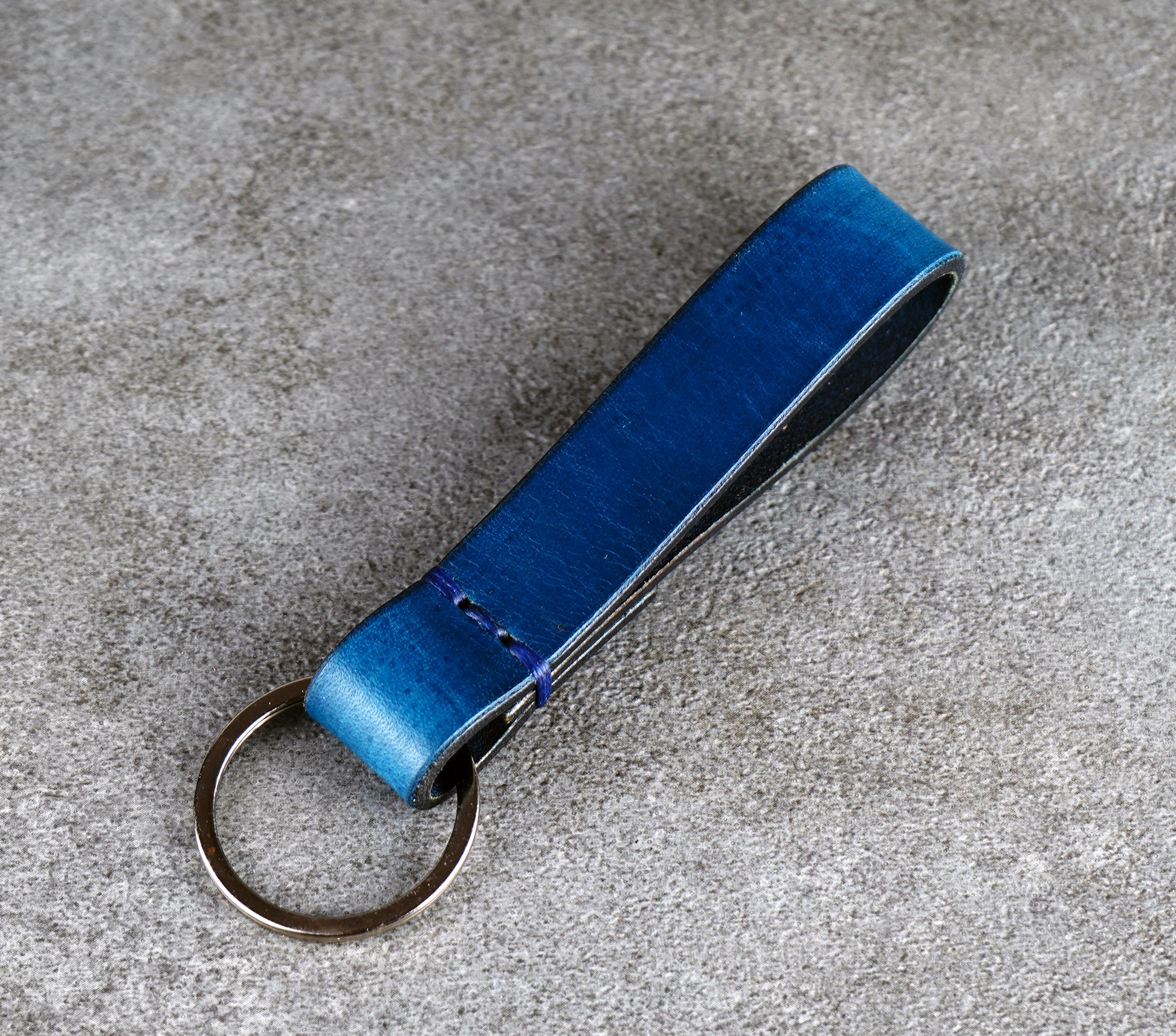 Blue leather keychain on a gray concrete surface