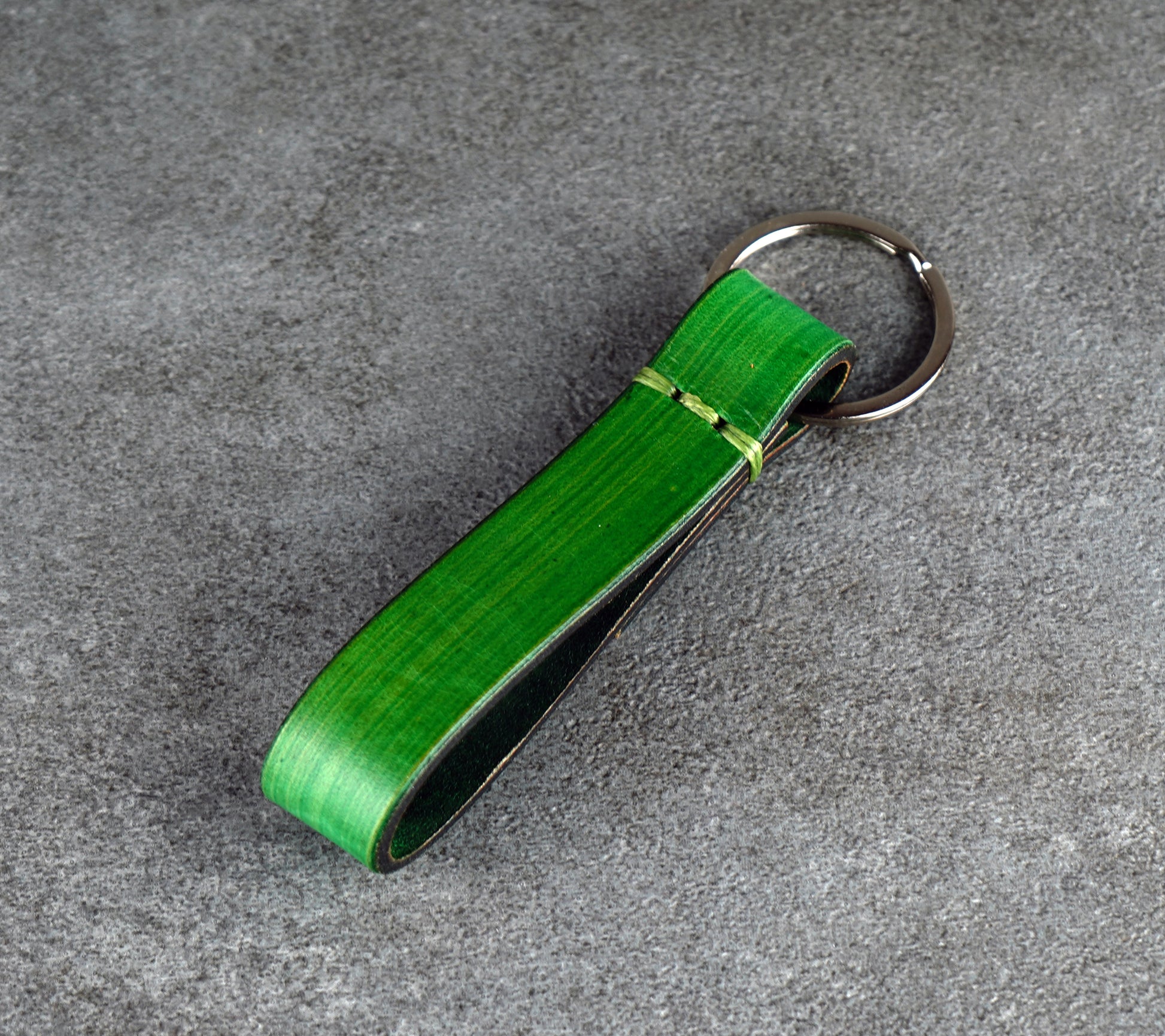 Green leather keychain with a metal clip on a gray surface