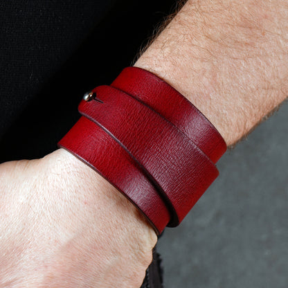 Wide red leather cuff bracelet wrapped twice around the wrist, handcrafted from smooth genuine leather with a bold minimalist design. Deep burgundy statement wristband accessory styled with black clothing for a modern edgy look.