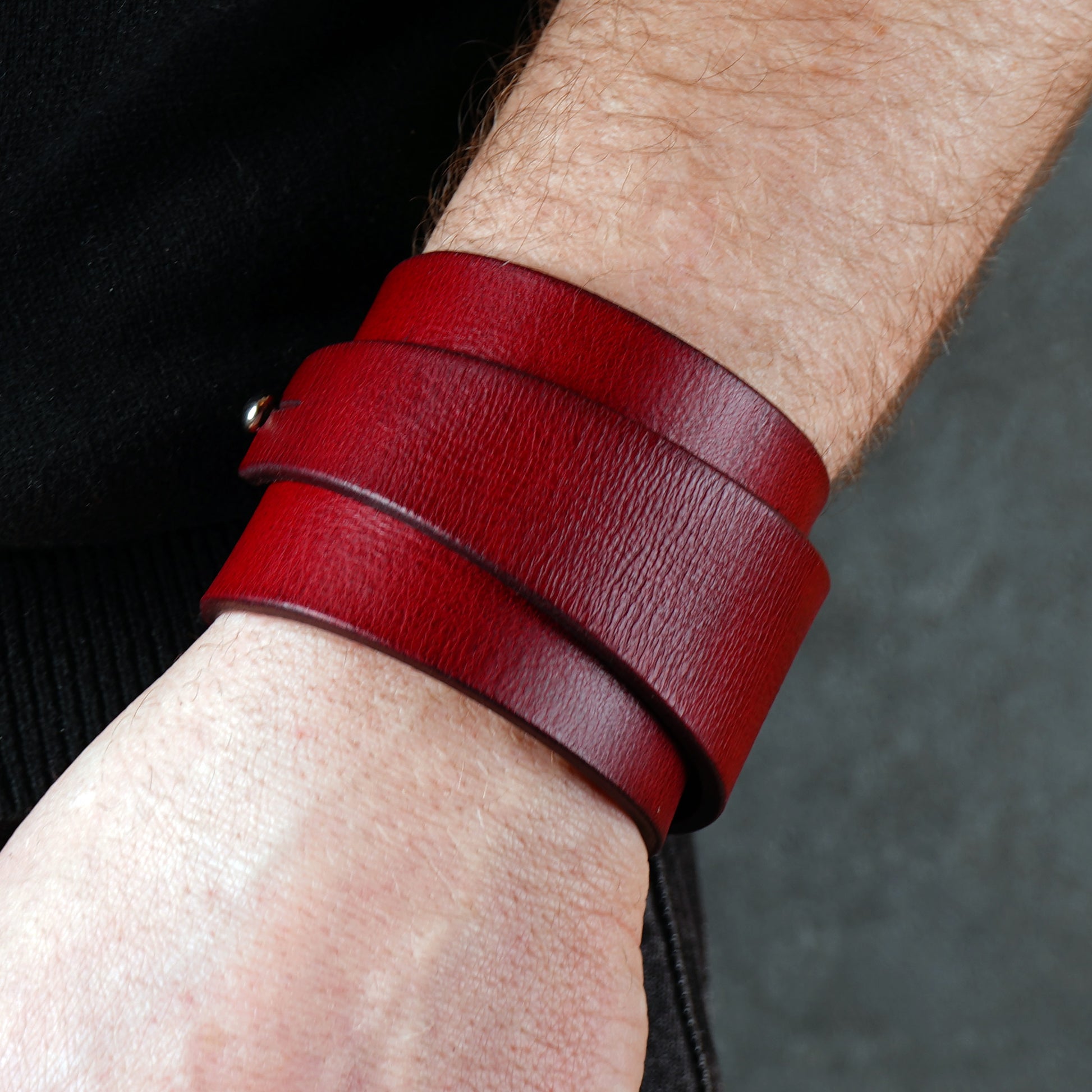 Wide red leather cuff bracelet wrapped twice around the wrist, handcrafted from smooth genuine leather with a bold minimalist design. Deep burgundy statement wristband accessory styled with black clothing for a modern edgy look.