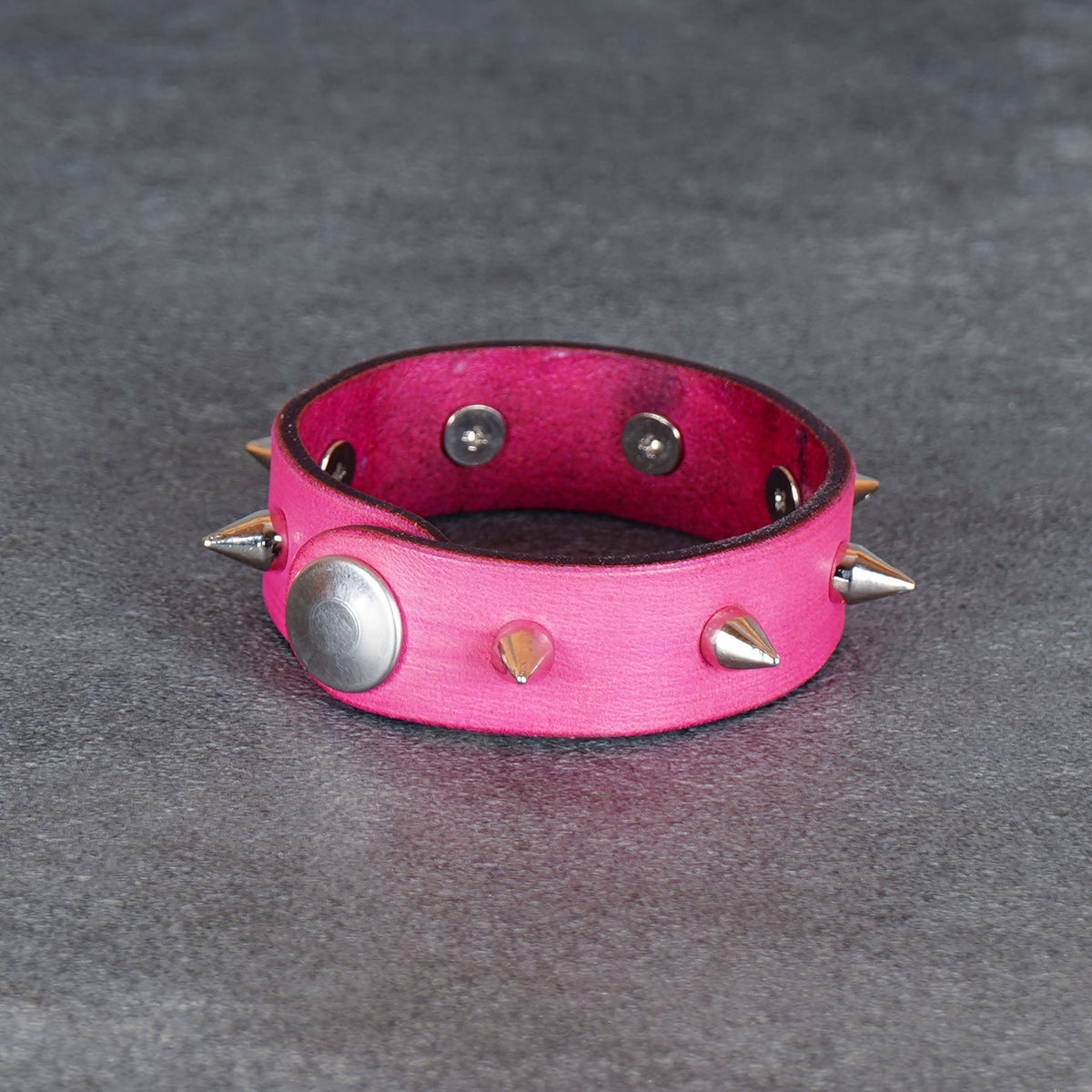 Pink spiked leather bracelet from a low front angle with the snap stud visible