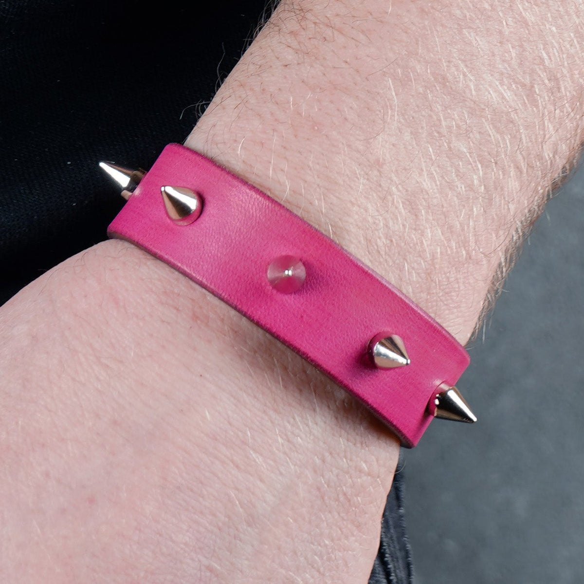 Pink spiked leather bracelet worn on a wrist from a close side angle