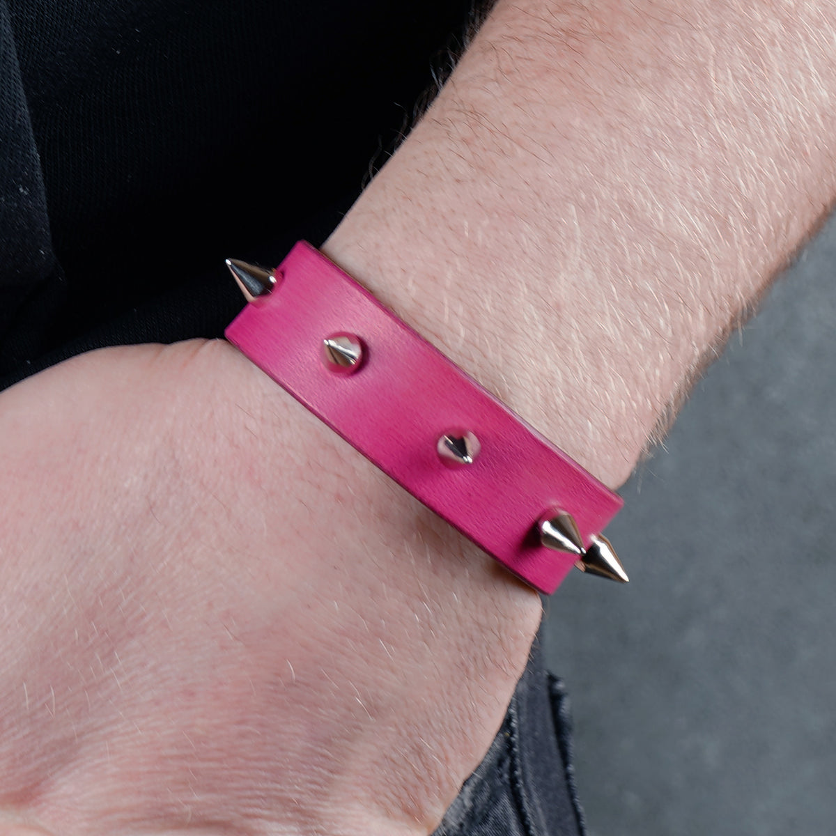 Pink spiked leather bracelet worn at an angle showing the strap length