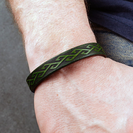 Green leather bracelet worn on a wrist, showing the engraved band near denim