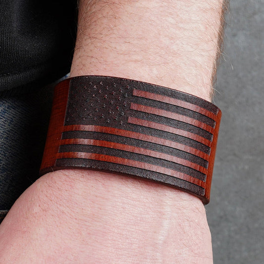 Brown leather cuff bracelet worn on a wrist with the flag design centered