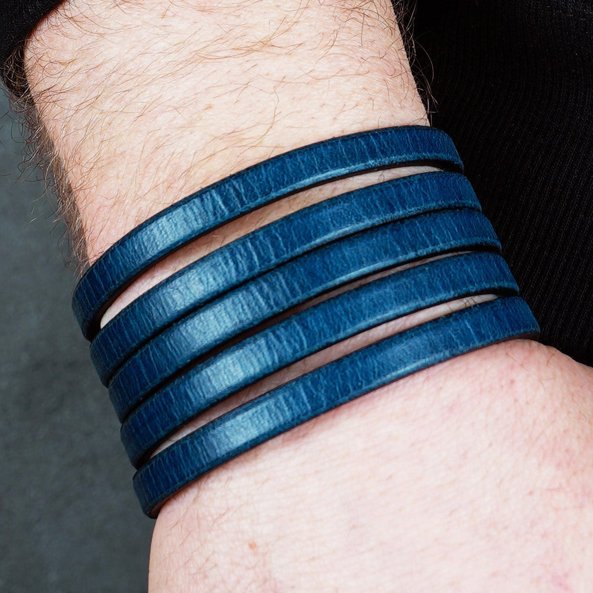 Blue leather wrap bracelet on gray background, handmade genuine leather cuff bracelet with layered strap design, minimalist blue wristband accessory for men and women
