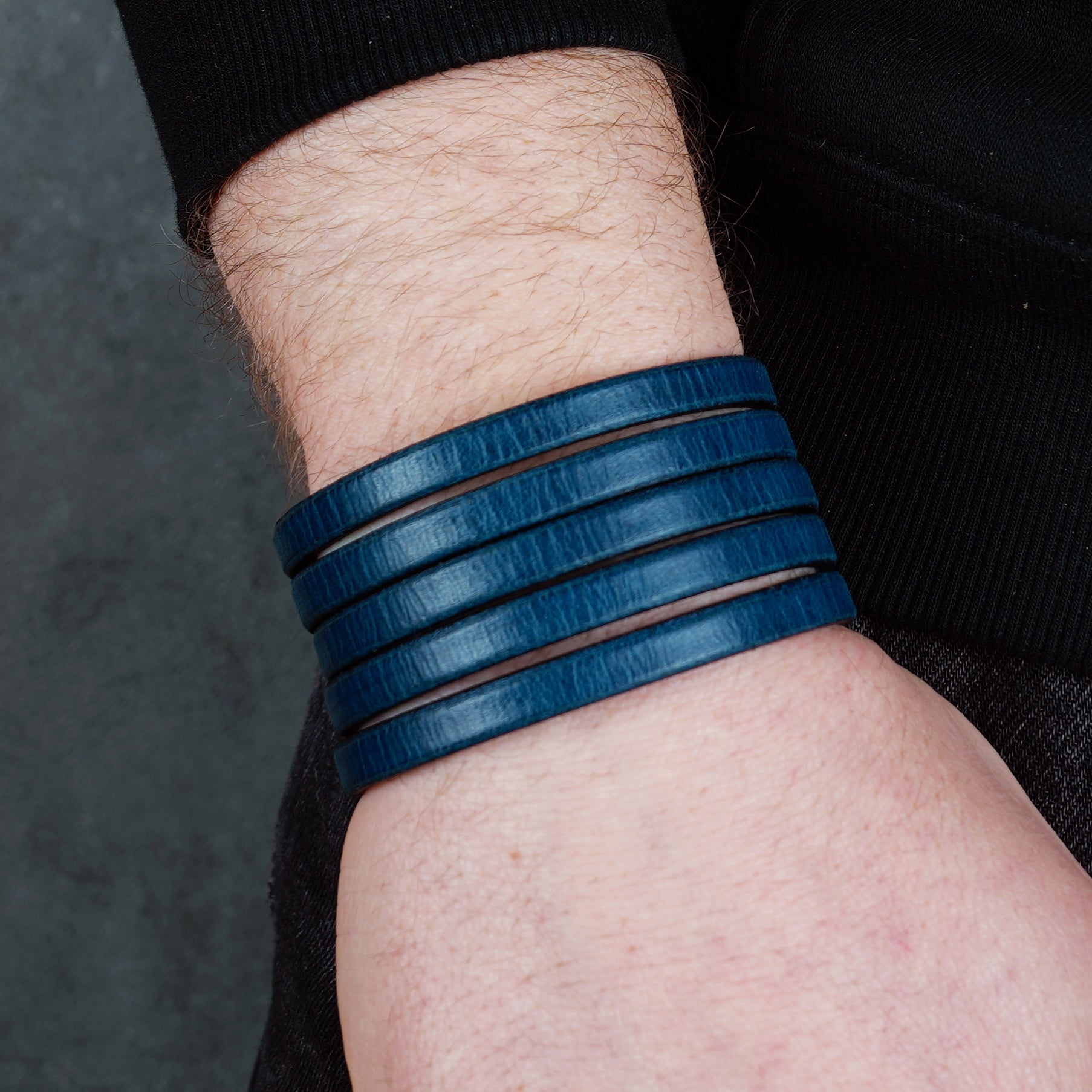 Blue leather wrap bracelet on gray background, handmade genuine leather cuff bracelet with layered strap design, minimalist blue wristband accessory for men and women
