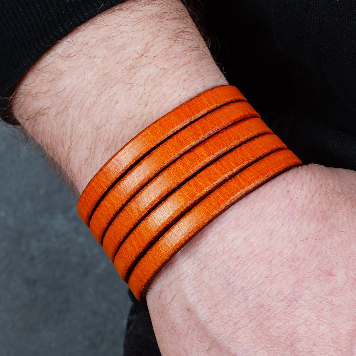 Orange leather cuff bracelet worn on a wrist from the opposite side