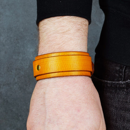 Yellow leather cuff bracelet on a wrist, with a brass rivet detail visible on the front.