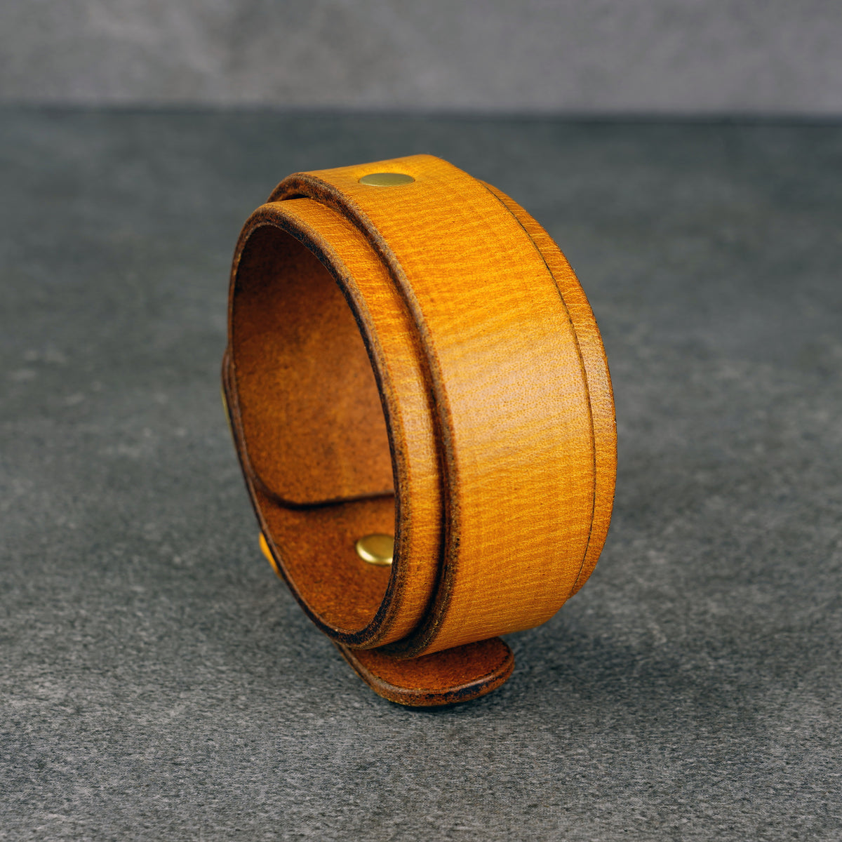Yellow leather cuff bracelet standing upright, showing the wide band and brass snap studs.