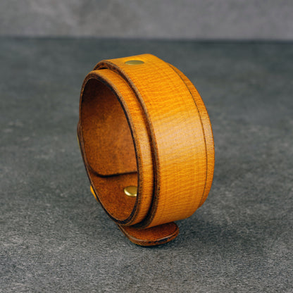 Yellow leather cuff bracelet standing upright, showing the wide band and brass snap studs.