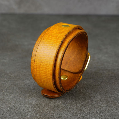 Yellow leather cuff bracelet standing upright, showing the wide band, brass buckle, and a visible snap detail.