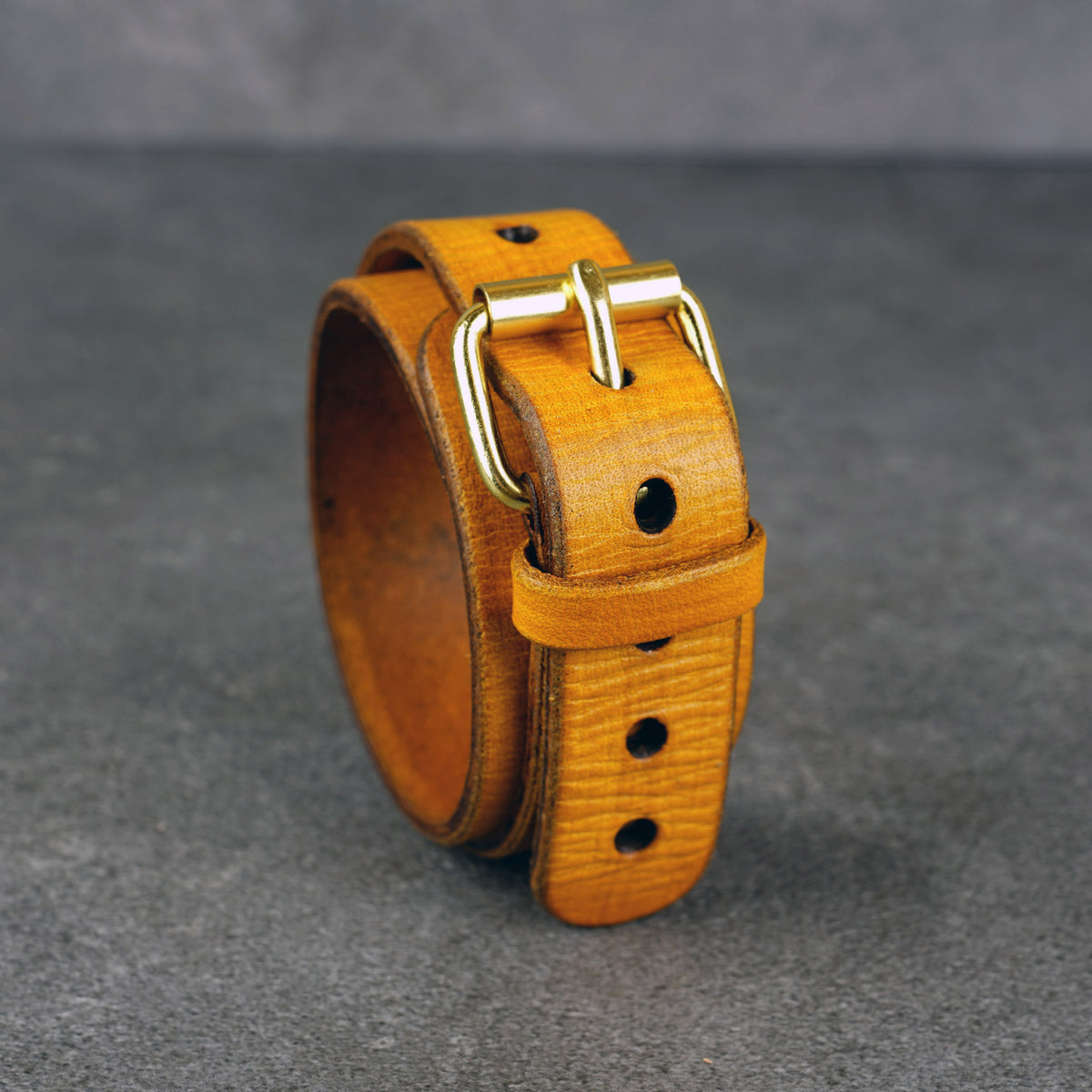 Yellow leather cuff bracelet standing upright with a brass buckle and punched adjustment holes.