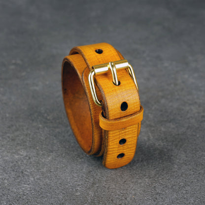 Yellow leather cuff bracelet standing upright, angled to show the brass buckle and punched holes.