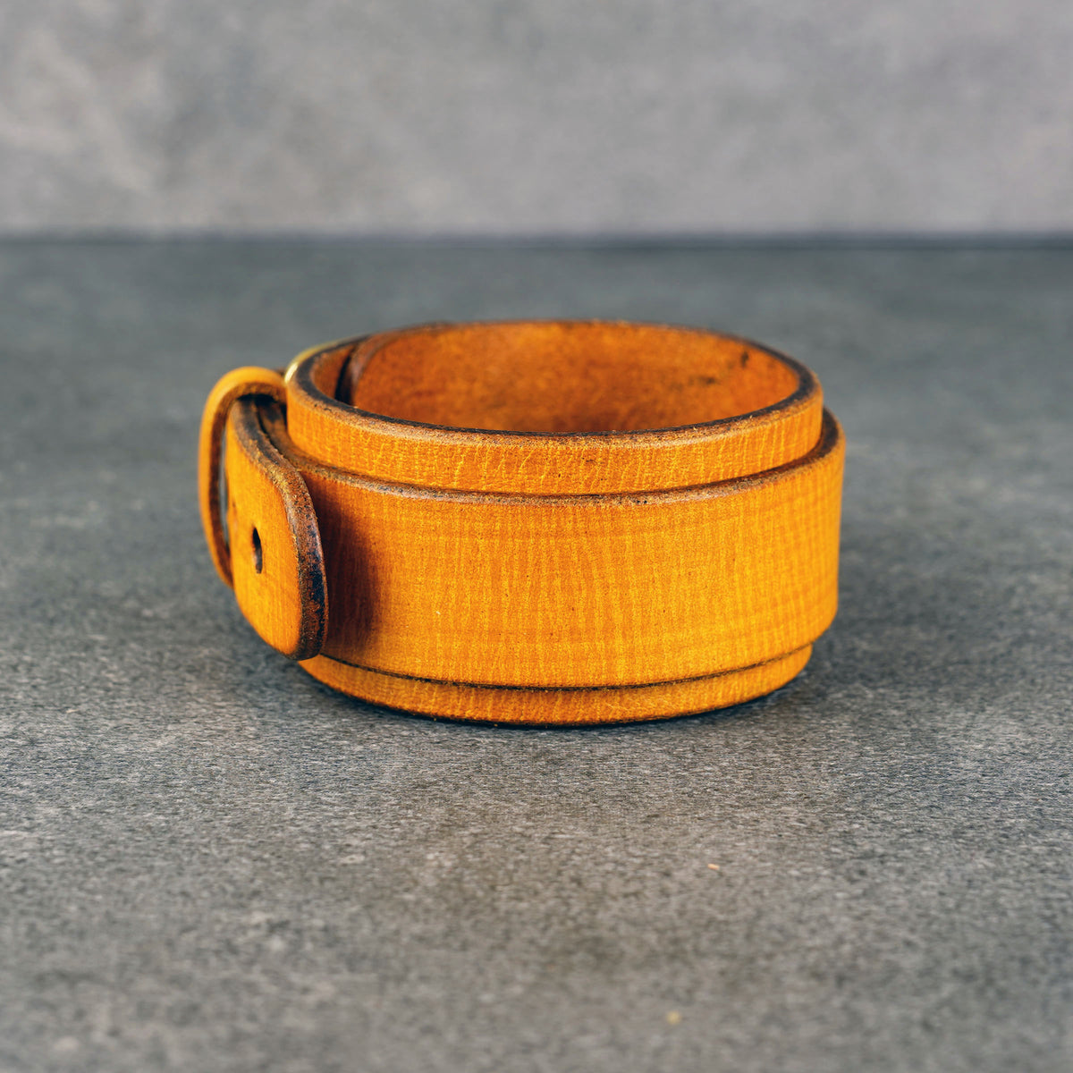 Yellow leather cuff bracelet standing upright, showing the side buckle tab and dark edge finish.