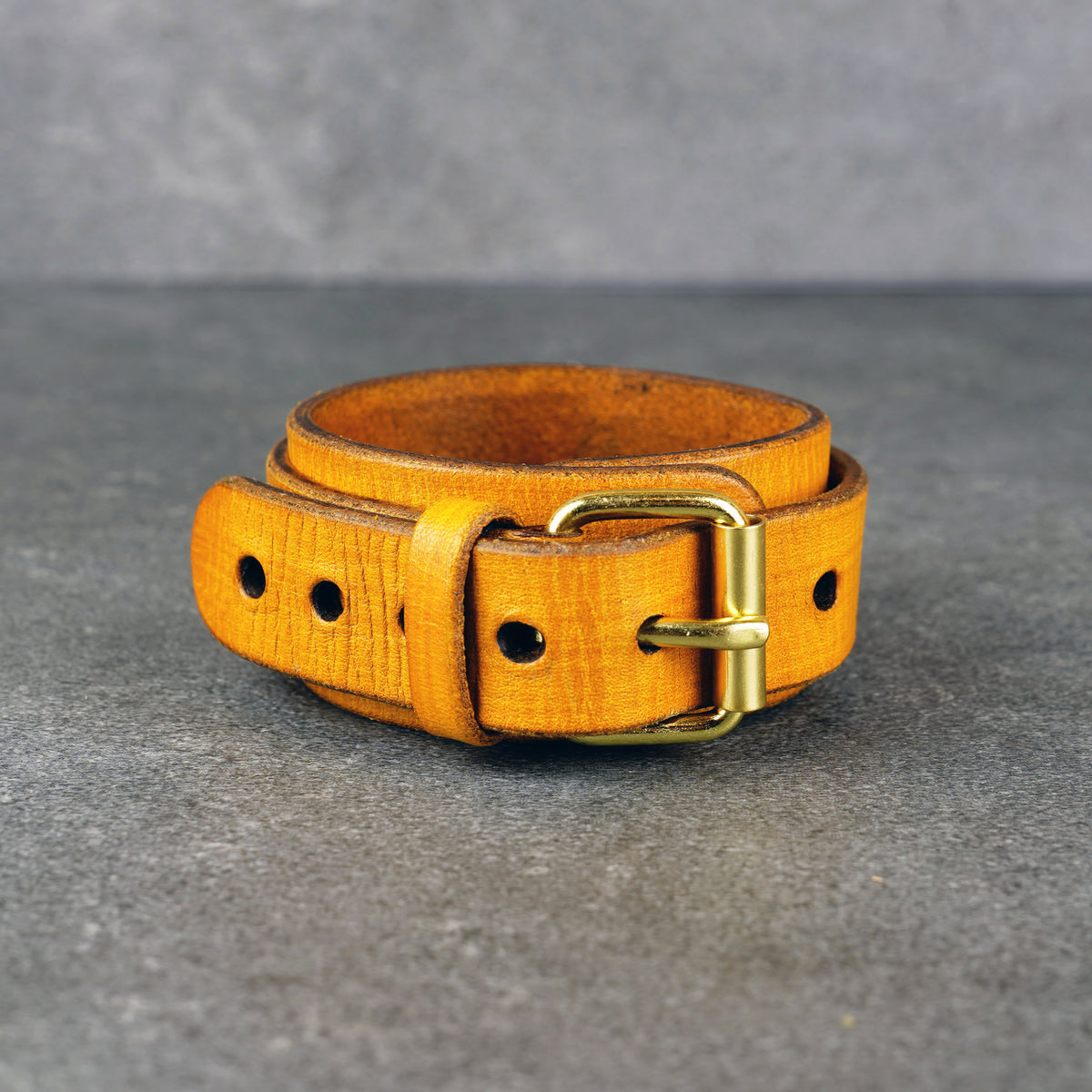 Yellow leather cuff bracelet standing upright with a brass buckle and punched holes visible on the front.