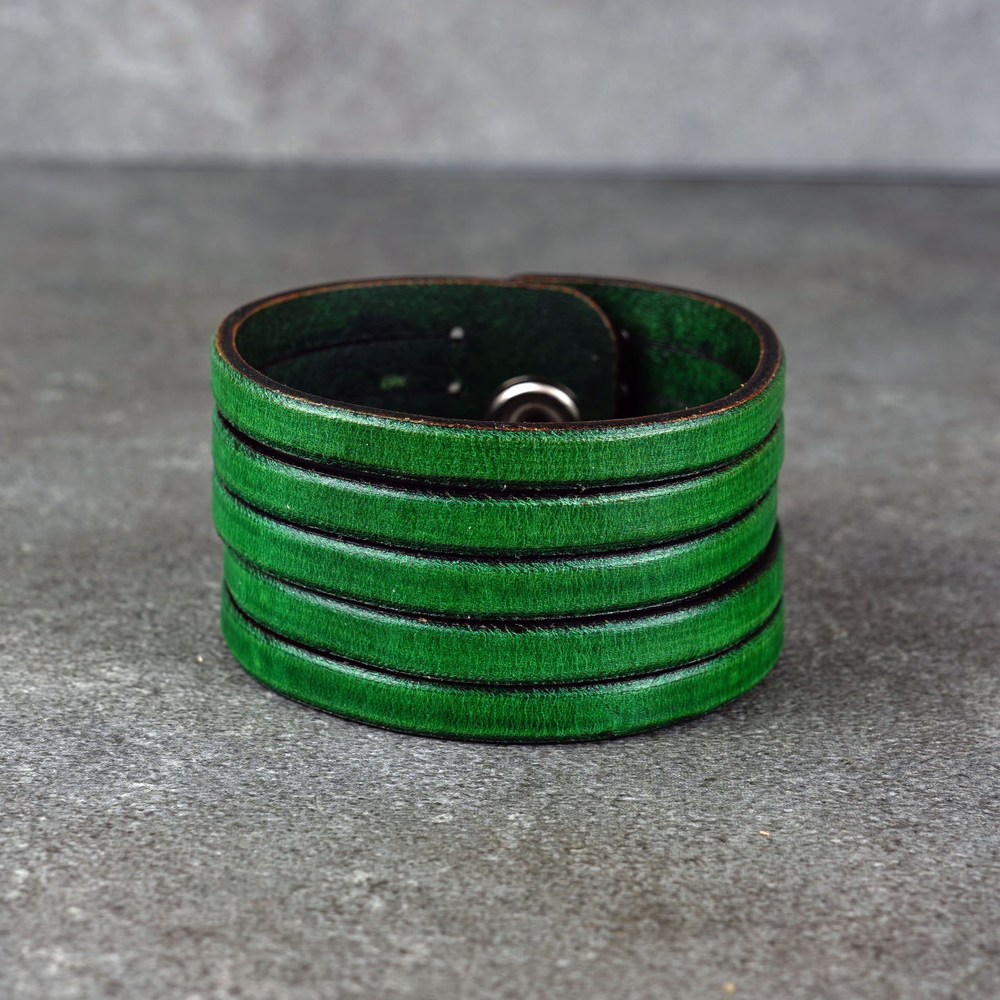 Green leather wrap bracelet on gray background, handmade genuine leather cuff bracelet with layered design, minimalist green wristband accessory for men and women
