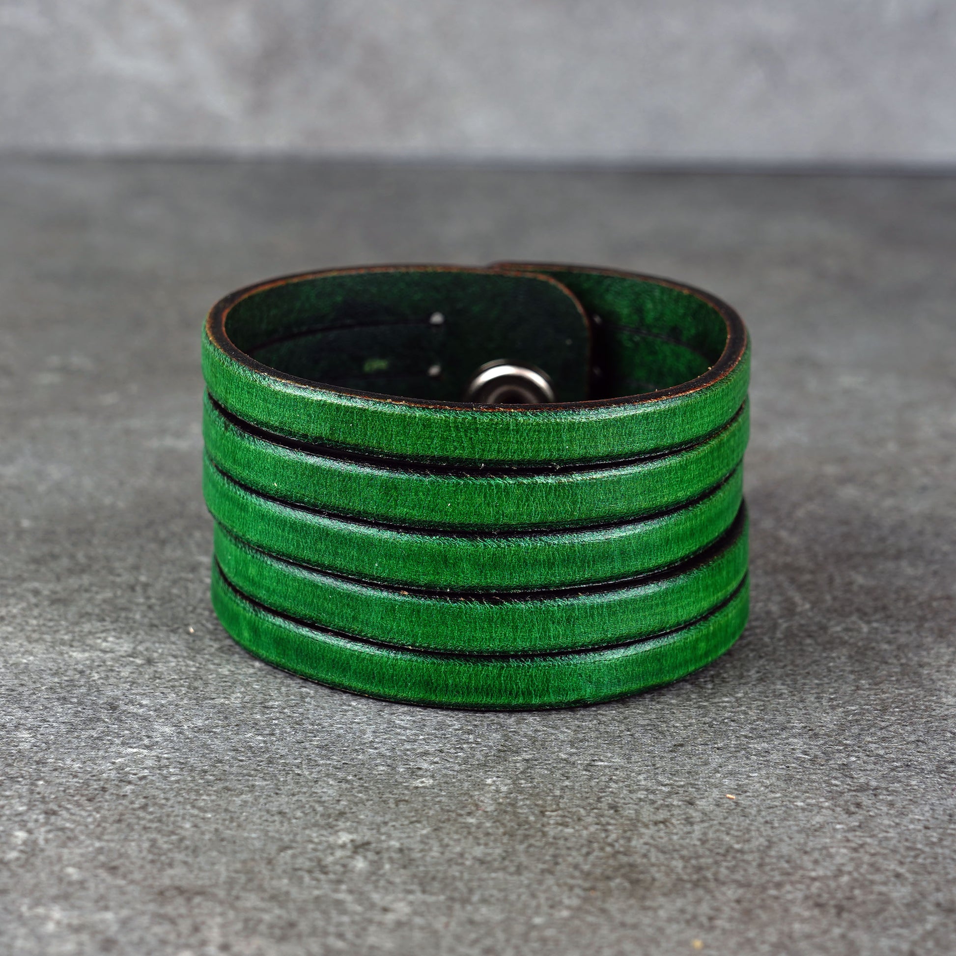 Green leather wrap bracelet on gray background, handmade genuine leather cuff bracelet with layered design, minimalist green wristband accessory for men and women
