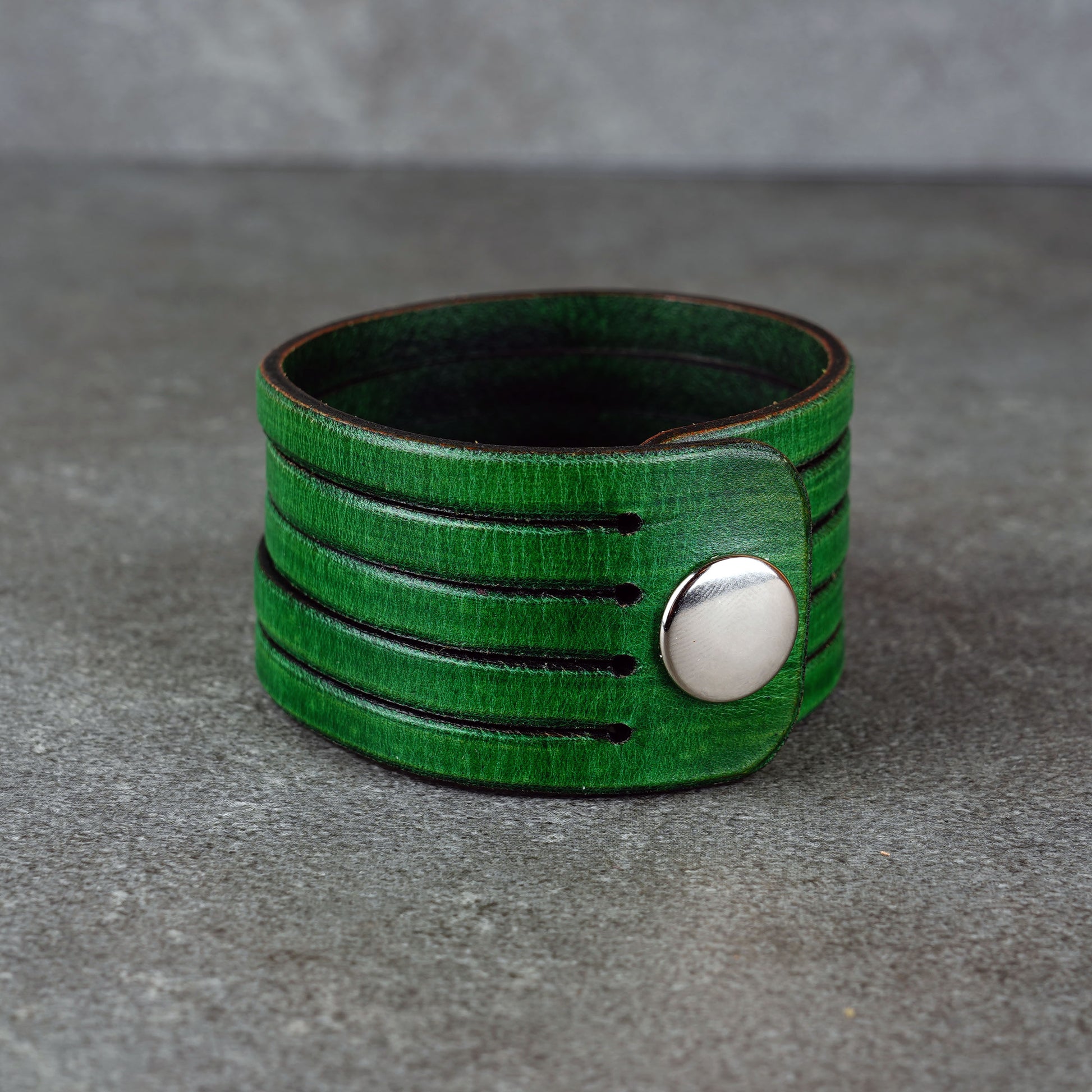 Green leather wrap bracelet on gray background, handmade genuine leather cuff bracelet with layered design, minimalist green wristband accessory for men and women
