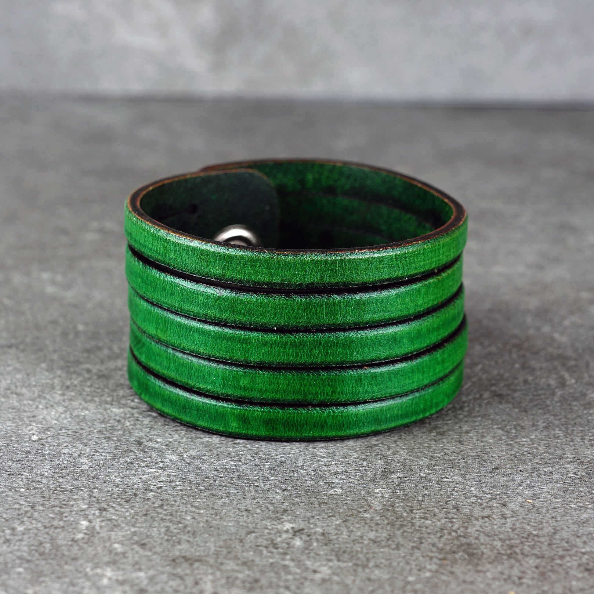 Green leather wrap bracelet on gray background, handmade genuine leather cuff bracelet with layered design, minimalist green wristband accessory for men and women
