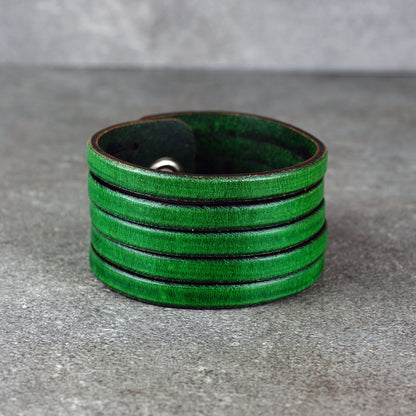 Green leather wrap bracelet on gray background, handmade genuine leather cuff bracelet with layered design, minimalist green wristband accessory for men and women
