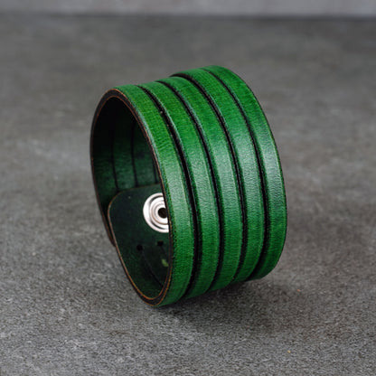 Green leather wrap bracelet on gray background, handmade genuine leather cuff bracelet with layered design, minimalist green wristband accessory for men and women
