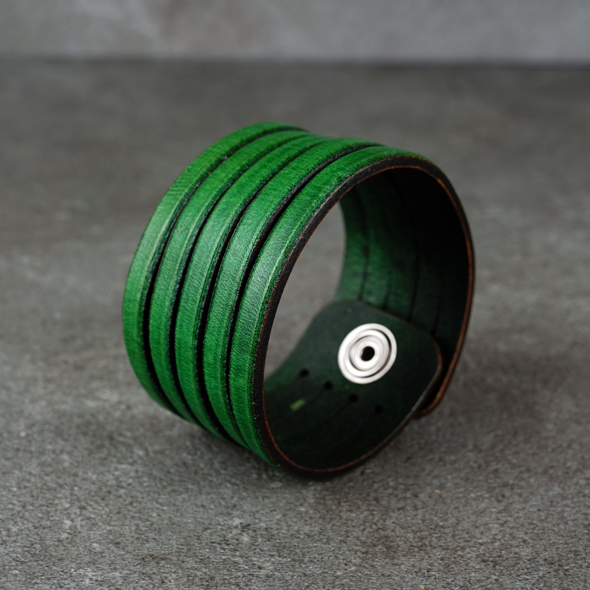 Green leather wrap bracelet on gray background, handmade genuine leather cuff bracelet with layered design, minimalist green wristband accessory for men and women
